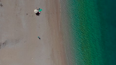 Ruhiger-Strand-Mit-Wenigen-Sonnenschirmen-Auf-Sand-In-Der-Nähe-Von-Smaragdgrünem-Meerwasser-Im-Mittelmeer