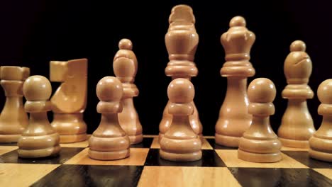 Truck-shot-from-left-to-right-of-white-chess-pieces-standing-on-a-chessboard-on-a-black-background