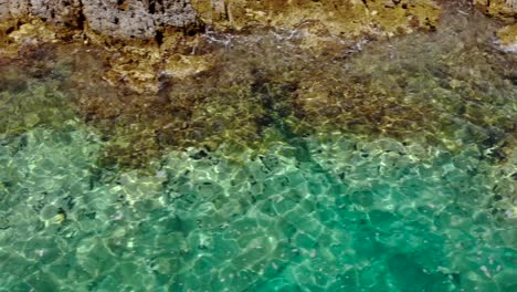 Smaragdgrüne-Meerwasserstruktur-Am-Meer-Mit-Felsen,-Die-Von-Ruhigem-Meerwasser-Umspült-Werden,-Das-Sonnenlicht-Reflektiert