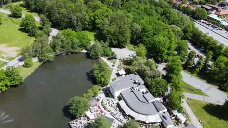 Calm-Lake-Surrounded-By-Green-Trees-Under-The-Vibrant-Sunlight-In-Slottsskogen-Park-In-Gothenburg,-Sweden---aerial-drone