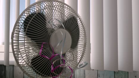 Static-shot-of-a-stopping-fan-in-the-background-of-closed-window-blinds