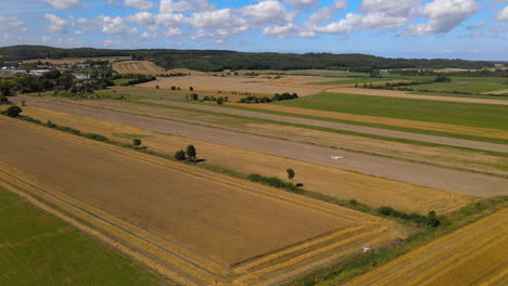 Drone-Pulls-Back-Revealing-Birds-Flying-Over-Magnificent-Countryside-Golden-and-Green-Fields-and-Meadows-with-Fluffy-Clouds