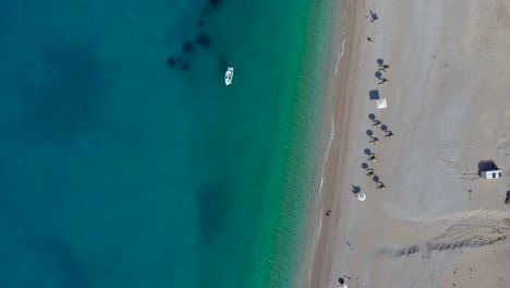 Strand-Mit-Sonnenschirmen-Auf-Sand,-Der-Von-Azurblauem-Meerwasser-Im-Mittelmeer-Umspült-Wird,-Sommerurlaub