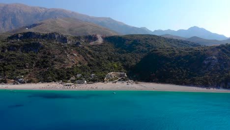 Hermosa-Playa-Panorámica-Vista-Desde-El-Agua-De-Mar-Azul-Celeste-Con-Fondo-De-Montañas-Albanesas