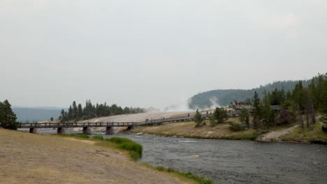 Tourists-Walking-On-The-Footbridge-With-Steam-Rising-On-The-Background-From-The-Grand-Prismatic-Spring-In-Yellowstone-National-Park,-Wyoming,-USA