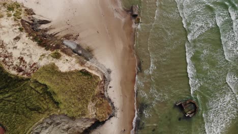 Aerial-top-down-view-of-epic-sand-beach-with-old-German-bunkers-laying-in-the-sand-and-water-while-the-wide-waves-hit-the-beach