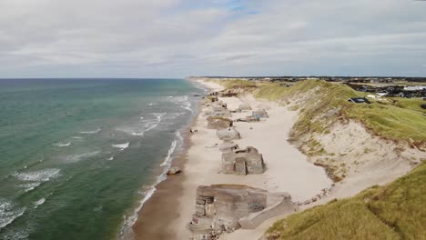 Aerial-dolly-in-of-old-house-located-close-to-the-white-sand-beach-on-the-Danish-west-coast-filled-with-old-abandoned-German-bunkers-from-world-war-2