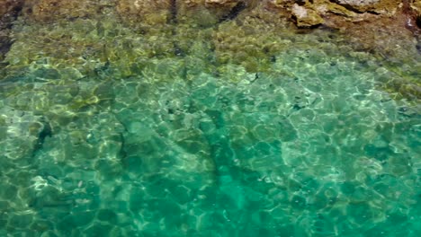 Kristallklares,-Smaragdgrünes-Meer-Am-Felsigen-Ufer,-Das-Den-Sonnenschein-Reflektiert,-Wassertextur-Als-Kopierraum