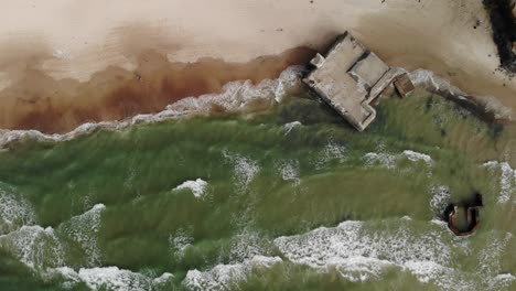 Aerial-top-down-view-of-waves-crashing-against-old-German-bunkers-from-world-war-2-located-on-a-beach-on-at-the-Danish-west-coast