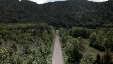 Infiniti-Car-Road-Trip-Across-The-Lush-Green-Driving-Trail-Heading-Towards-The-Scenic-Mountain-On-A-Sunny-Day---Drone-Shot