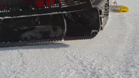 Close-up-of-a-snow-groomer-passing-by,-starting-at-front-with-shovel,-tracked-tires-and-roller-in-back,-creating-fresh-new-slope-with-corduroy-pattern,-slow-motion