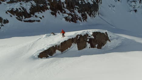 Skier-wearing-red-jacket-taking-leap-of-faith-from-rocky-cliff,-extreme-sport