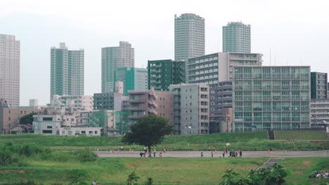 Japanese-Children-Playing-At-The-Park-In-Tamagawa-With-High-Rise-Buildings-In-The-Background-In-Tokyo,-Japan---wide-shot