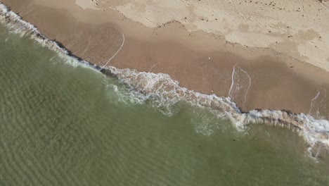 Aerial-shot-of-clear-ocean-small-waves-crashing-on-a-white-sand-beach