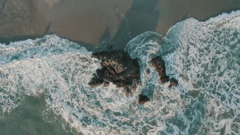 Aerial-drone-top-view-of-rocks-in-the-sea,-zooming-out-revealing-the-beach-in-Costa-Rica