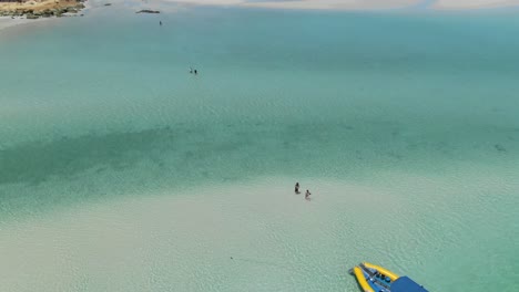 Aerial-forward-over-tourists-walking-in-shallow-transparent-waters,-Whitehaven-beach