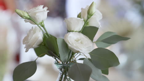 White-roses-in-glass-vase-blowing-in-wind-at-wedding-party