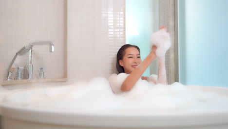 Woman-taking-a-hot-bath-relaxing-in-a-bathtub-filled-with-foam-inside-a-hotel-room