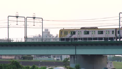 JR-Train-Passing-By-On-The-Bridge-In-Tamagawa-With-Cars-Parked-Under-In-Tokyo,-Japan---panning-shot