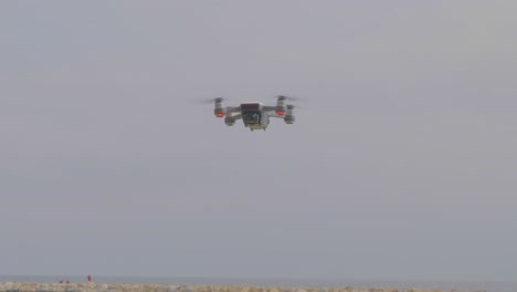 A-closeup-view-of-a-flying-drone-camera,-blinking-lights-and-turning-at-the-beach