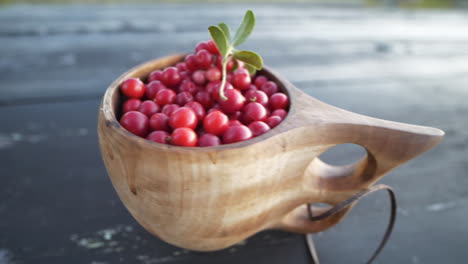 Lingonberries-in-a-wooden-cup-on-table,-close-up-panning-shot