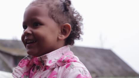Portrait-of-joyful-little-African-girl-looking-around-in-countryside-background