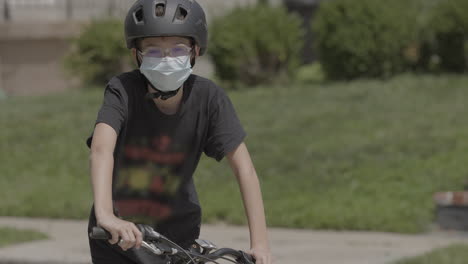 Medium-portrait-of-a-kid-on-a-bike-wearing-a-medical-mask-and-looking-into-camera