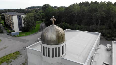Golden-dome-cupola-and-ornate-cross-on-top-of-roof-of-church-in-residential-community-and-neighborhood-with-scenic-green-trees-on-cloudy-blue-sky-day,-circle-aerial