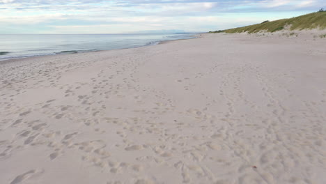 Luftbild:-Sehr-Langsamer-Flug-über-Sandstrand-Mit-Fußabdrücken-Und-Meeresküste-An-Der-Seite