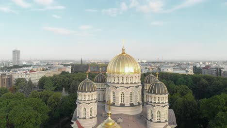 Spinning-aerial-view-of-Latvian-Nativity-of-Christ-cathedral-in-Esplanade-park-on-sunny-summer-day,-Riga-cityscape-in-background
