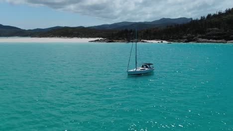 A-White-Sail-Boat-Sits-in-Turquoise-Ocean-Waters-off-the-coast-of-White-Haven-Beach,-Whitsundays-Australia