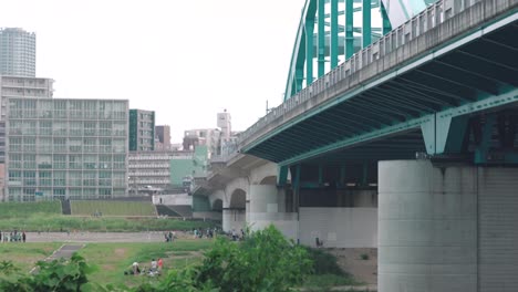 Marukobashi-Brücke-über-Den-Tamagawa-Fluss-Mit-Japanischen-Kindern,-Die-Im-Vordergrund-In-Tokio,-Japan,-Fußball-Spielen
