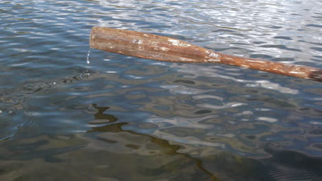 Wooden-oar-sweeping-into-rippling-water-on-lake,-slow-motion-shot