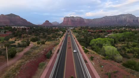 Aerial-view-of-cars-on-highway-179-in-Chapel,-the-Bell-rock-and-red,-sandstone-mountains-in-the-background,-Sedona,-Arizona,-USA---dolly,-drone-shot