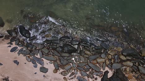 Drone-vertical-tracking-shot-of-rocky-coastline-and-beach-with-small-waves