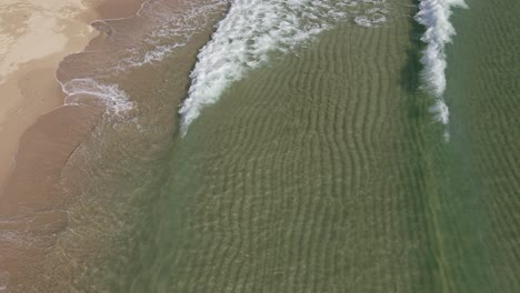 Aerial-static-shot-of-small-clear-tropical-ocean-waves-breaking-on-the-white-sand-beach