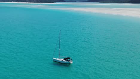 White-Sail-boat-Sits-Anchored-in-Clear-Green-Waters-off-the-Coastline-of-Queenslands-Whitehaven-beach,-Australia,-Drone-Aerial