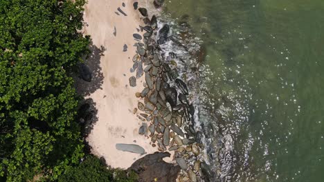 Aerial-downward-pan-shot-of-beach,-jungle-and-rocky-coastline