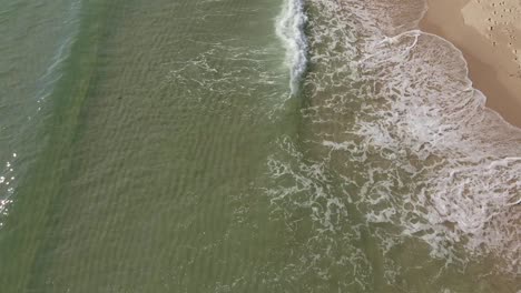 Drone-Pan-shot-of-small-waves-breaking-on-white-sand-beach-with-clear-water