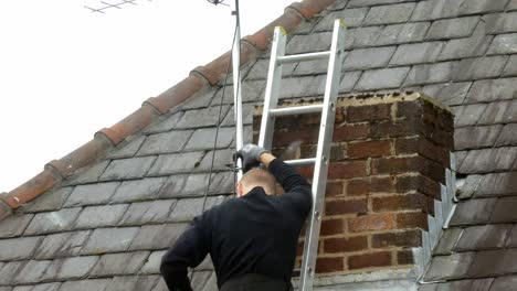 Man-on-ladder-fitting-television-aerial-on-home-chimney-roof