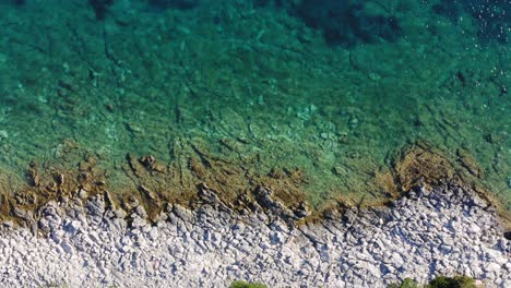 Aerial-top-view-of-rocky-shore-with-crystal-clear-turquoise-calm-water