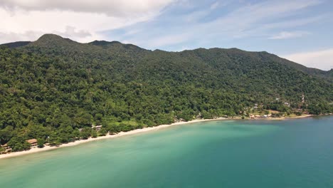 Aerial-shot-of-long-tropical-white-sand-beach-with-small-resorts-and-rain-Forrest-jungle-mountains-behind