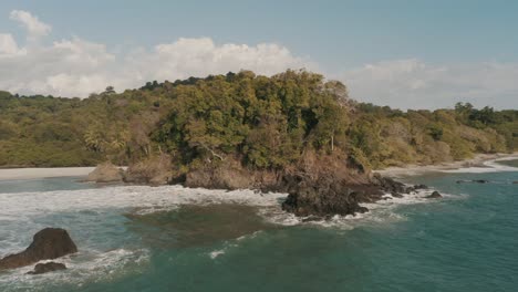Drohnenantenne-Von-Wellen,-Die-Auf-Einer-Klippe-Zusammenbrechen,-Mit-Palmen,-Die-Den-Strand-In-Costa-Rica-Enthüllen