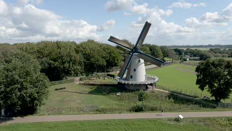 Flying-away-from-rotating-windmill,-revealing-beautiful-green-meadows