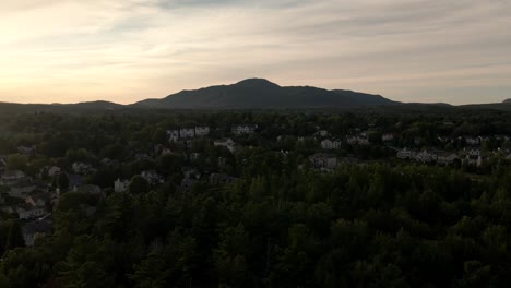 Revealing-Shot-Of-Hotel-Buildings-Behind-Lush-Trees-At-The-Beach-Front-Of-Lake-Memphremagog-In-Quebec,-Canada-At-Dawn---aerial-drone-ascend