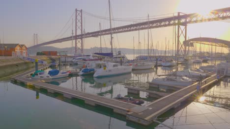 Ein-Wunderschöner-Majestätischer-Blick-Auf-Den-Hafen-Mit-Kleinen-Booten-Unter-Der-Abril-Brücke-Bei-Sonnenuntergang,-Lissabon,-Portugal