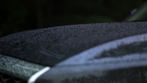 Rain-falls-onto-Hood-of-Black-car-and-creates-Water-Droplets-that-run-off,-Extreme-Close-Up,-Focus-Pull