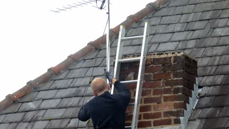 Man-working-on-ladder-installing-digital-television-aerial-on-home-roof