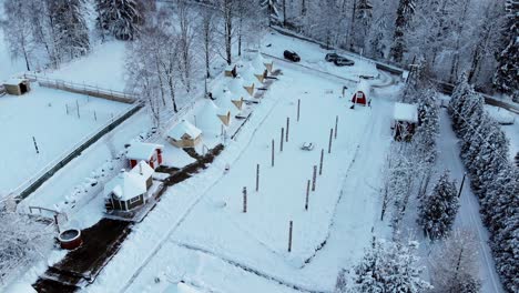 Aerial-view-overlooking-cabins-in-a-Finnish-holiday-village,-in-middle-of-arctic-forest,-on-a-cloudy,-winter-day---orbit,-drone-shot