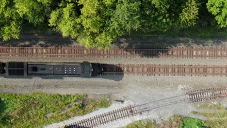 Black-diesel-locomotive-train-engine-with-headlight-on,-stopped-on-railroad-track,-top-down-overhead-aerial-drone-perspective,-switching-car,-track,-freight-and-travel-transportation-concept